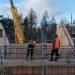 A photo of the MAKAR prototype house during construction. Two men in hi-vis vests and hard hats are standing on scaffolding and a crane can be seen in the background.