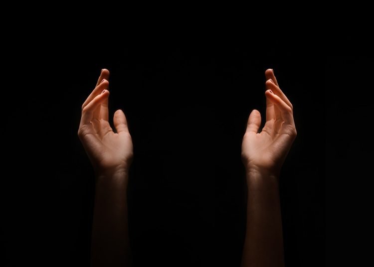 This image shows two hands reaching upward in the dark. The hands are positioned symmetrically, with their palms facing upwards.