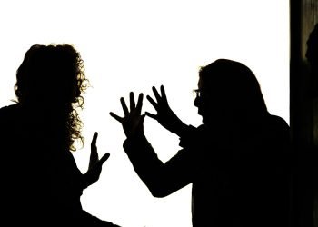 A silhouetted woman is being shouted at by a silhouetted man, The man has his hands raised, the woman has one hand in front of her in a stop motion